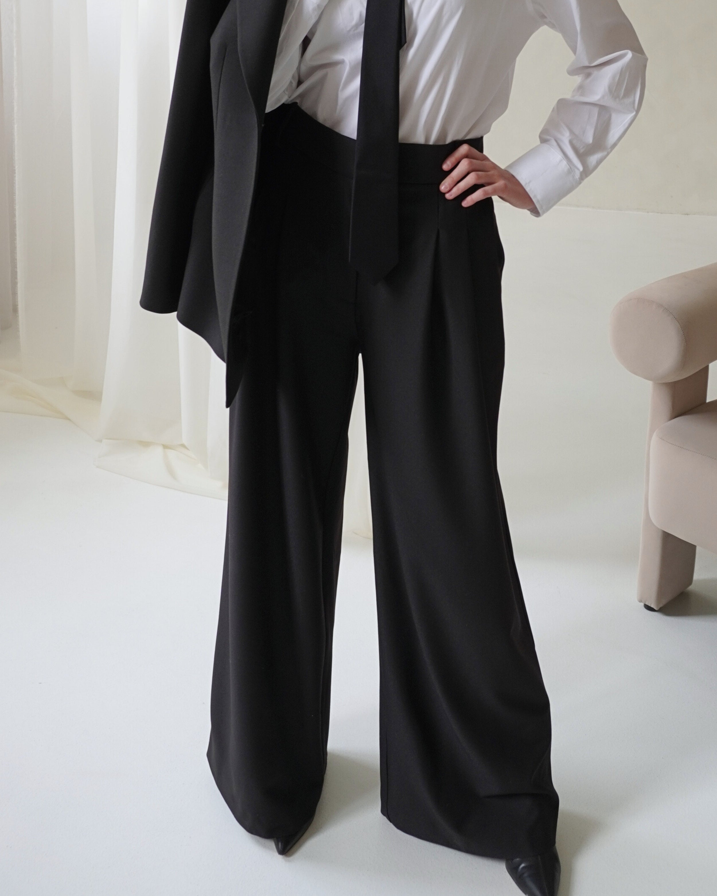 Model wearing THÉFI Dione high-waist wide-leg trousers in black.