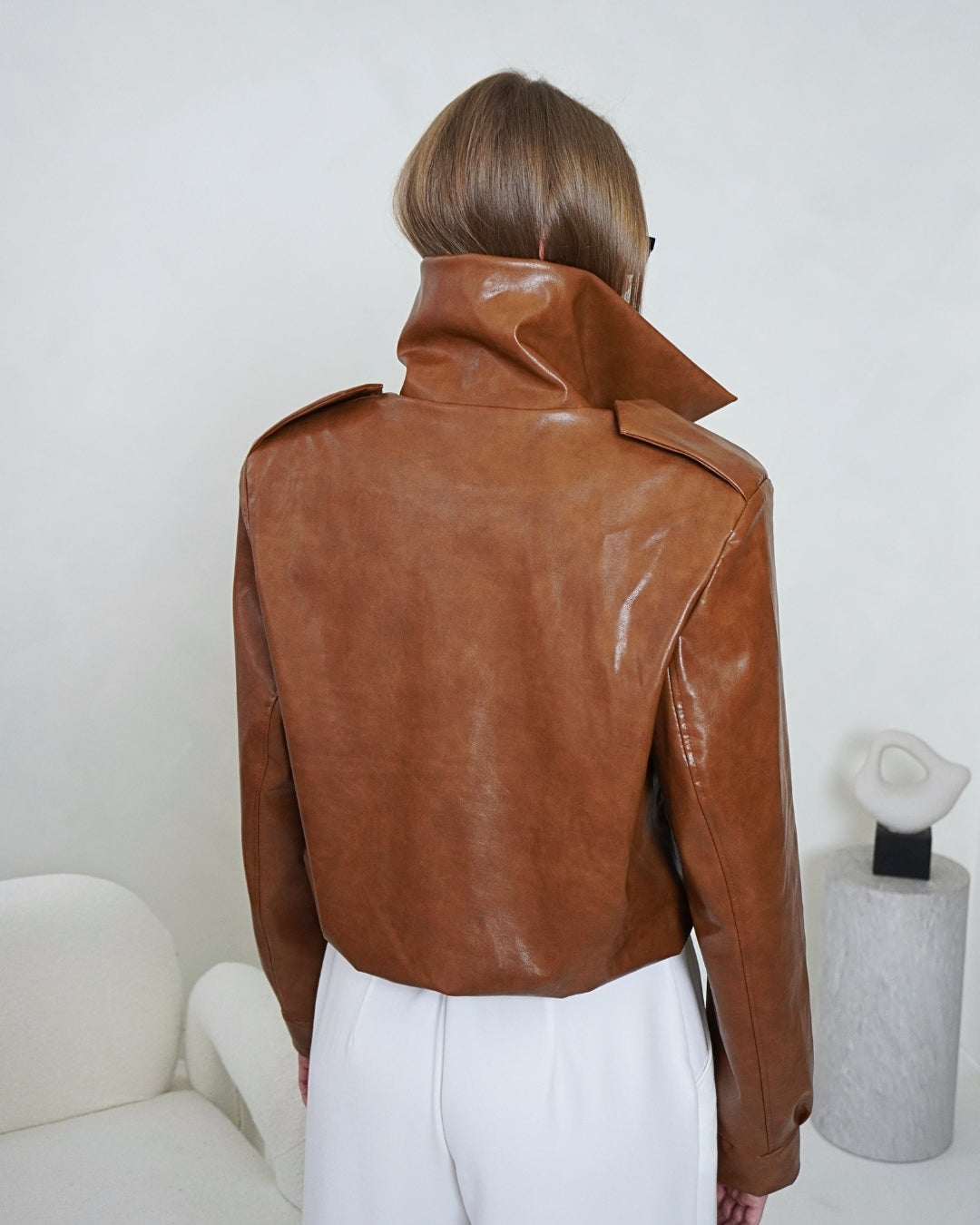 Back view of the brown HERA Faux Leather Jacket by THÉFI, showing the structured shoulders, high collar and gathered hem.
