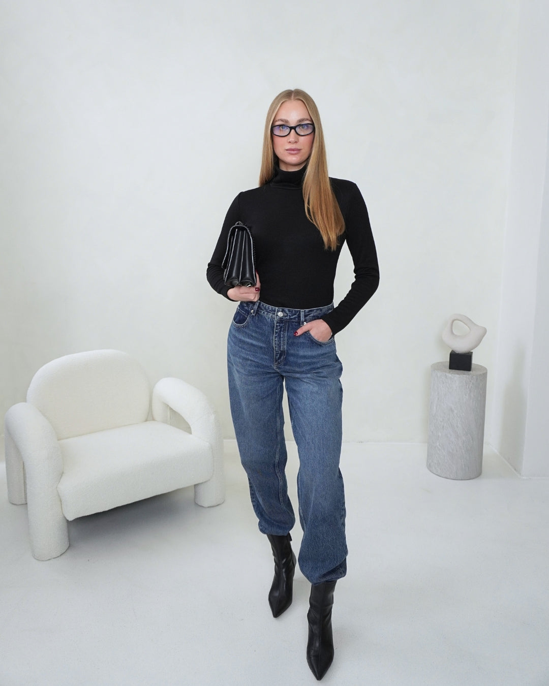 Full-length view of the black SELENE Turtleneck by THÉFI styled with blue jeans, black ankle boots and a black handbag.