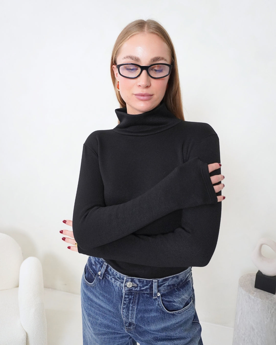 Model wearing the black SELENE Turtleneck with arms crossed, showing its elongated sleeves, fitted silhouette and high neckline.