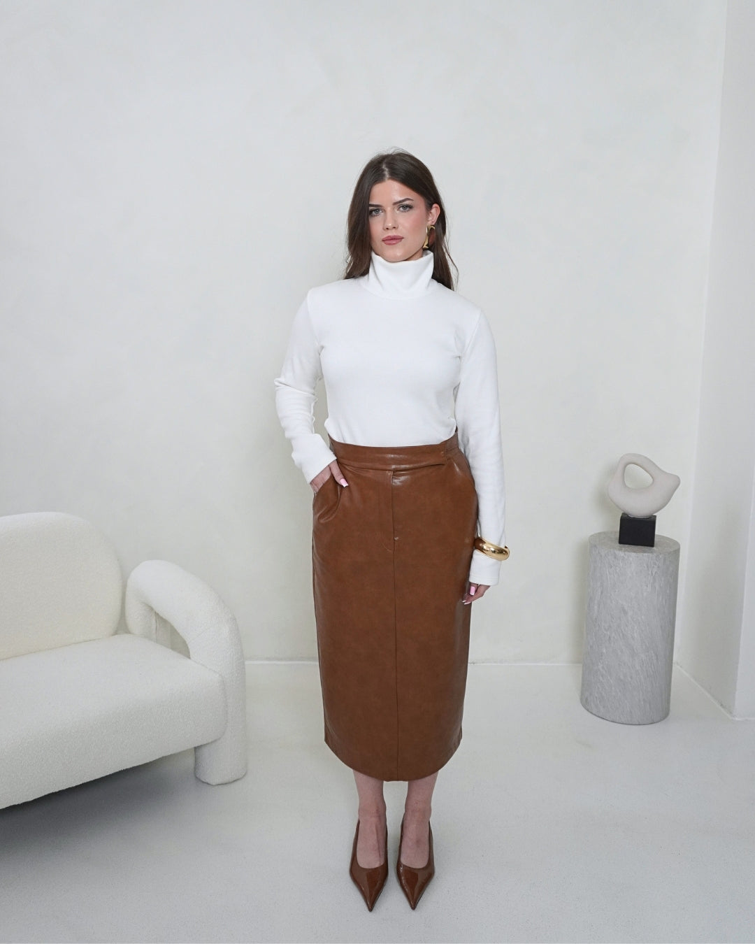 Full-length front view of the cream SELENE Turtleneck styled with the brown THALIA Faux Leather Pencil Skirt and pointed-toe heels.