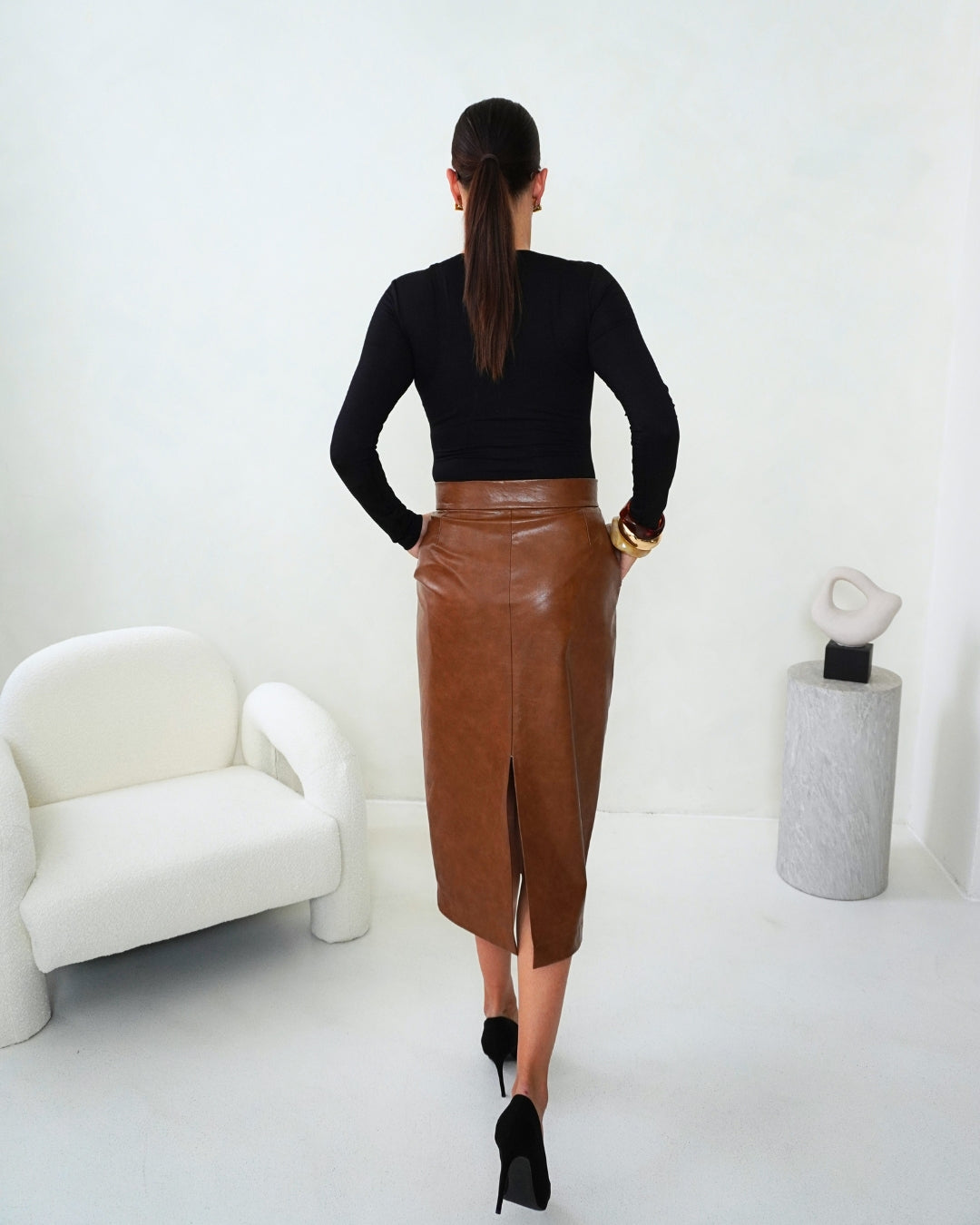 Back view of the brown THALIA Faux Leather Pencil Skirt with a fitted black top, showing its high-waisted shape and back slit.