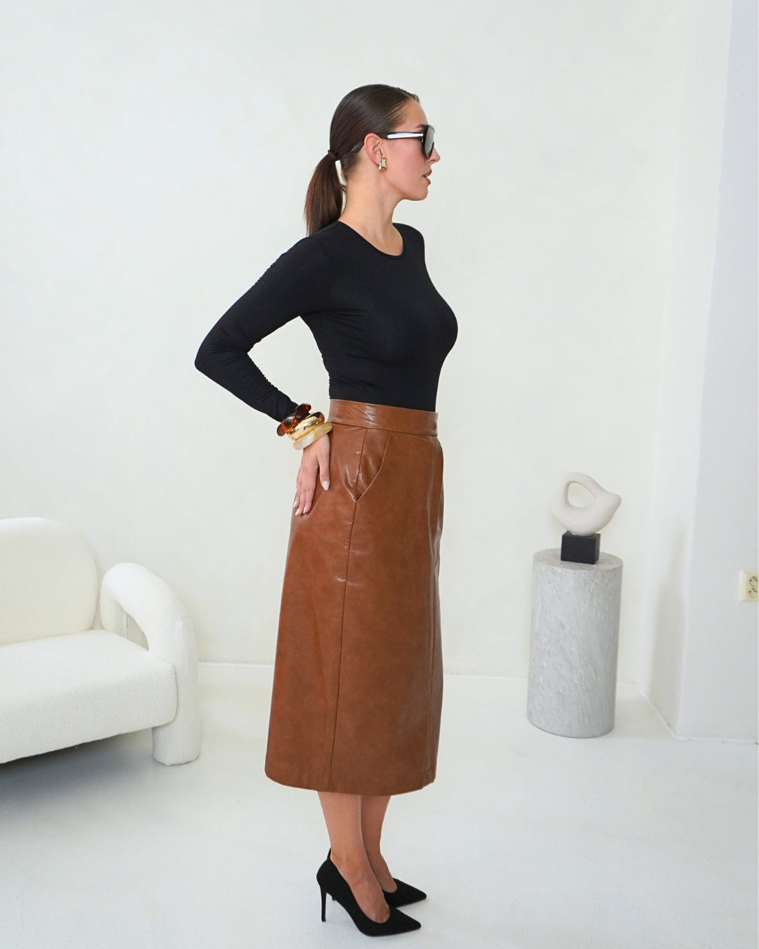 Side view of the brown THALIA Faux Leather Pencil Skirt styled with a black fitted top, showing the high waist and midi-length silhouette.