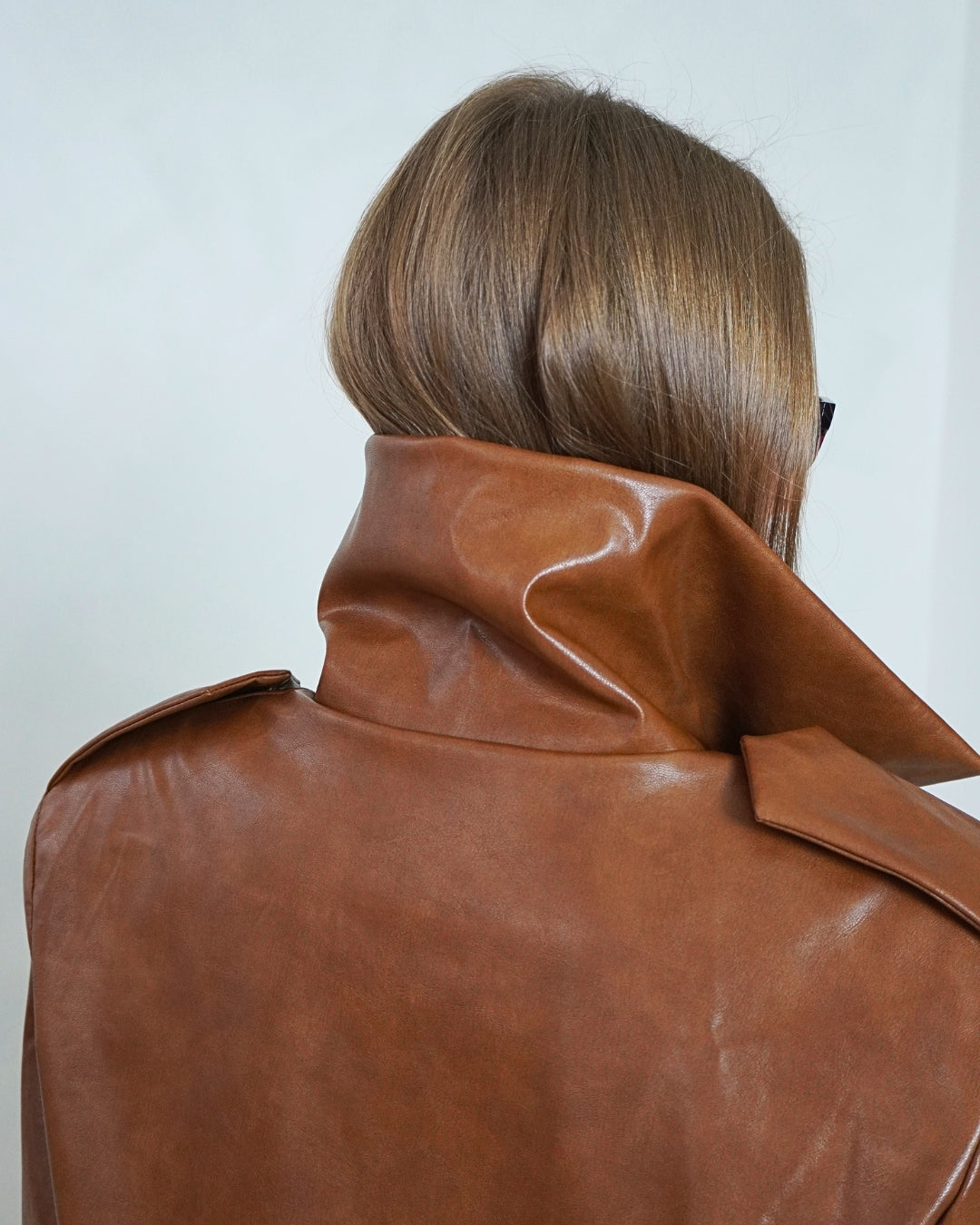 Close-up back view of the brown HERA Faux Leather Jacket, highlighting the high funnel neck and faux leather texture.