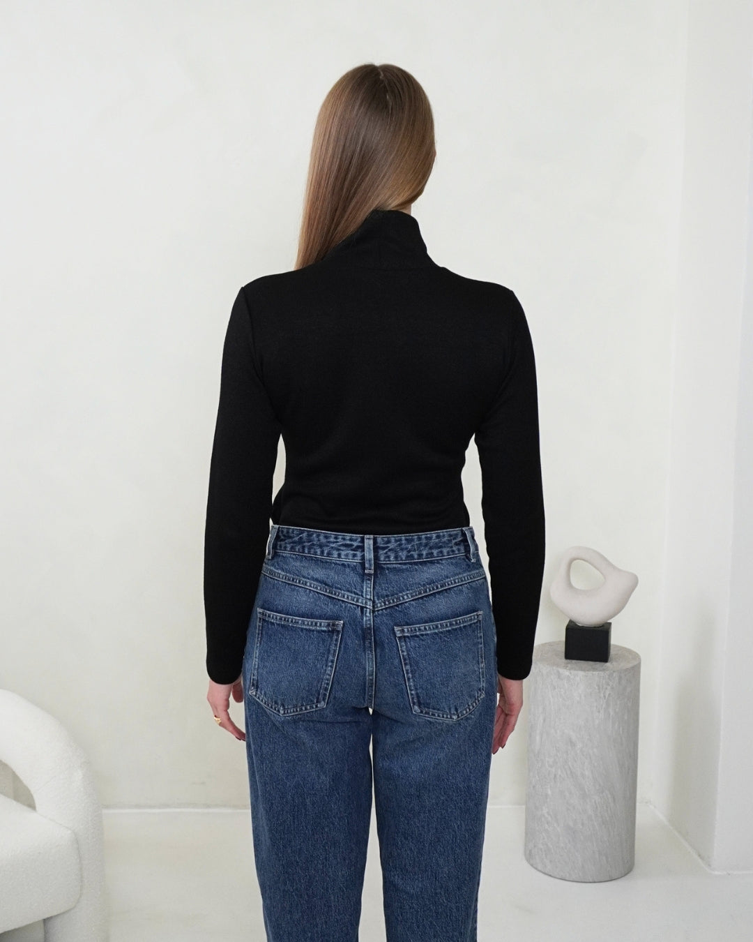 Back view of the black SELENE Turtleneck styled with blue jeans, showing the fitted silhouette and high collar.